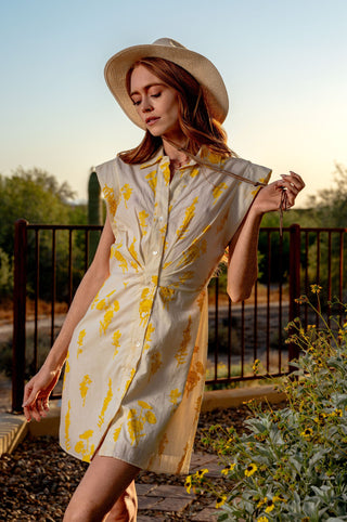 Woman in a yellow and white dress with a straw hat standing in a garden.